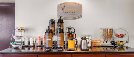 A breakfast bar with coffee makers, a coffee pot, and a fruit bowl.