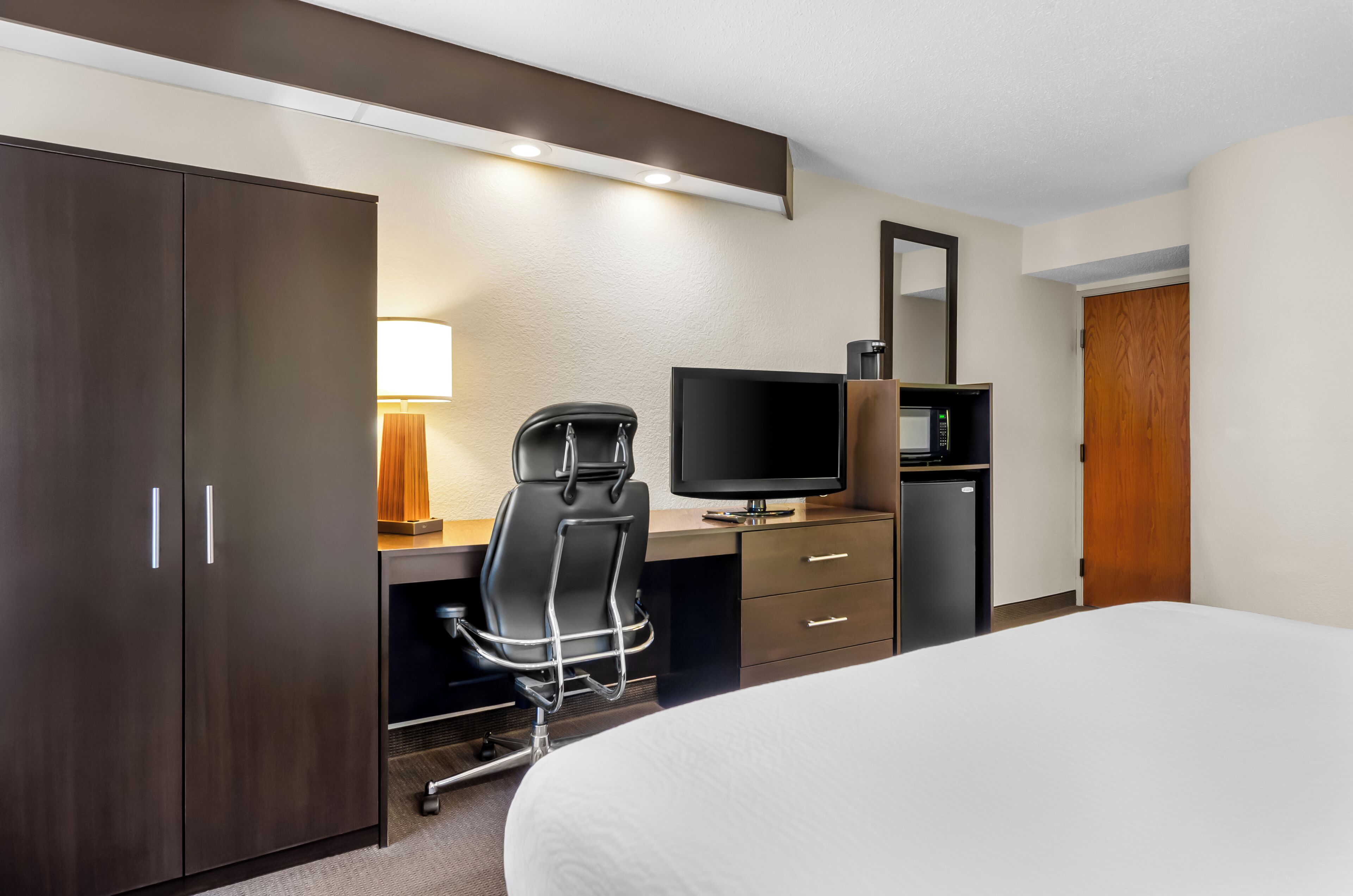 A hotel room with a bed, a desk with a chair, a television, a microwave, and a wardrobe.