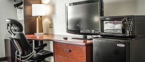 Habitación de hotel con un escritorio de madera, una silla de oficina negra, un televisor de pantalla plana, un microondas y un refrigerador pequeño.