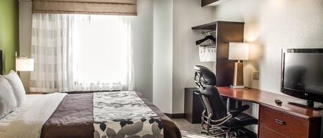 Une chambre d’hôtel avec un lit, un bureau, une chaise, une télévision et une fenêtre avec des rideaux.