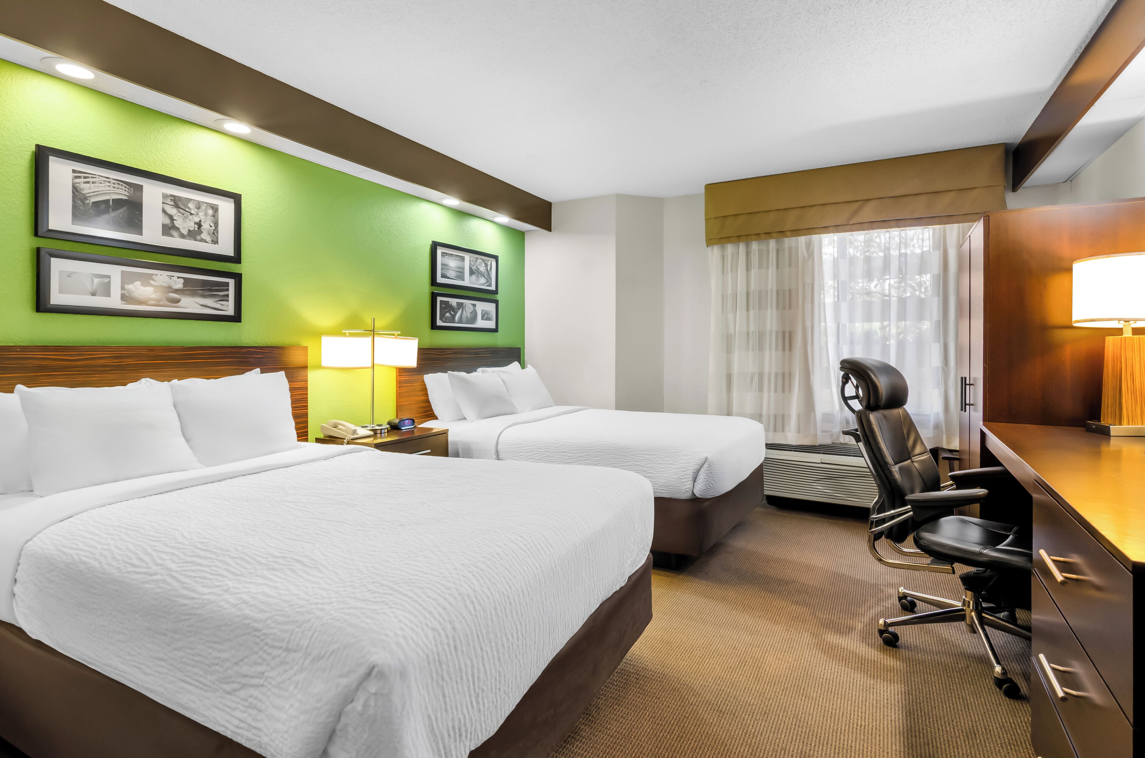 Habitación de hotel con dos camas, un escritorio, una silla y un ventanal con cortinas.