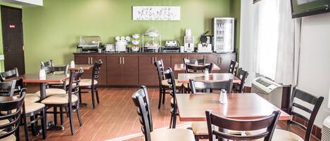 A dining area with multiple tables and chairs, a kitchen counter with appliances, and a television mounted on the wall.