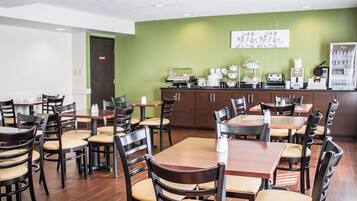 A dining area with multiple tables and chairs, a kitchen counter with appliances, and a green wall with a floral artwork.
