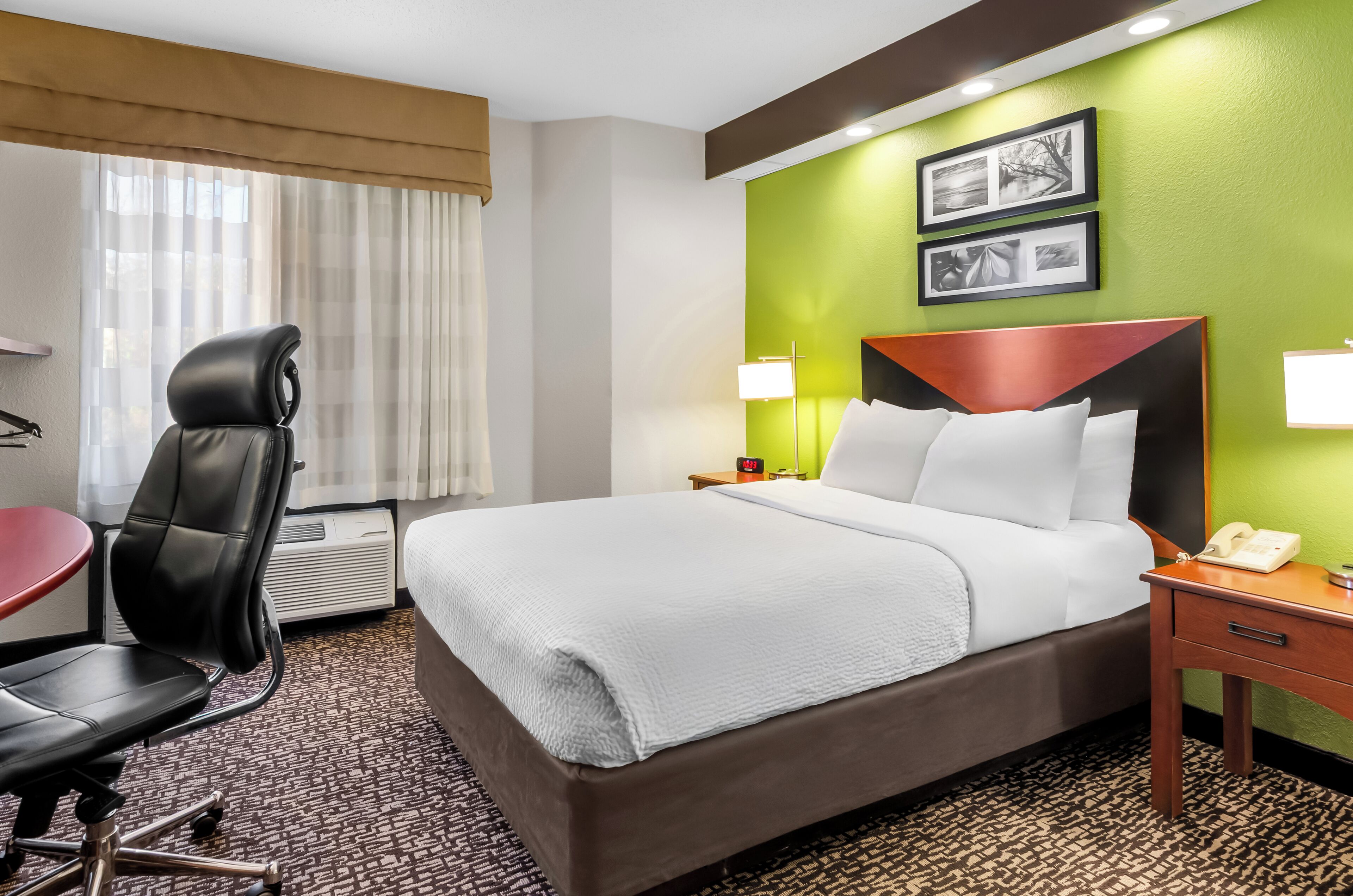 A hotel room with a large bed, a desk, a chair, and a lamp.
