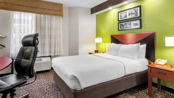A hotel room with a large bed, a desk, a chair, and a lamp.
