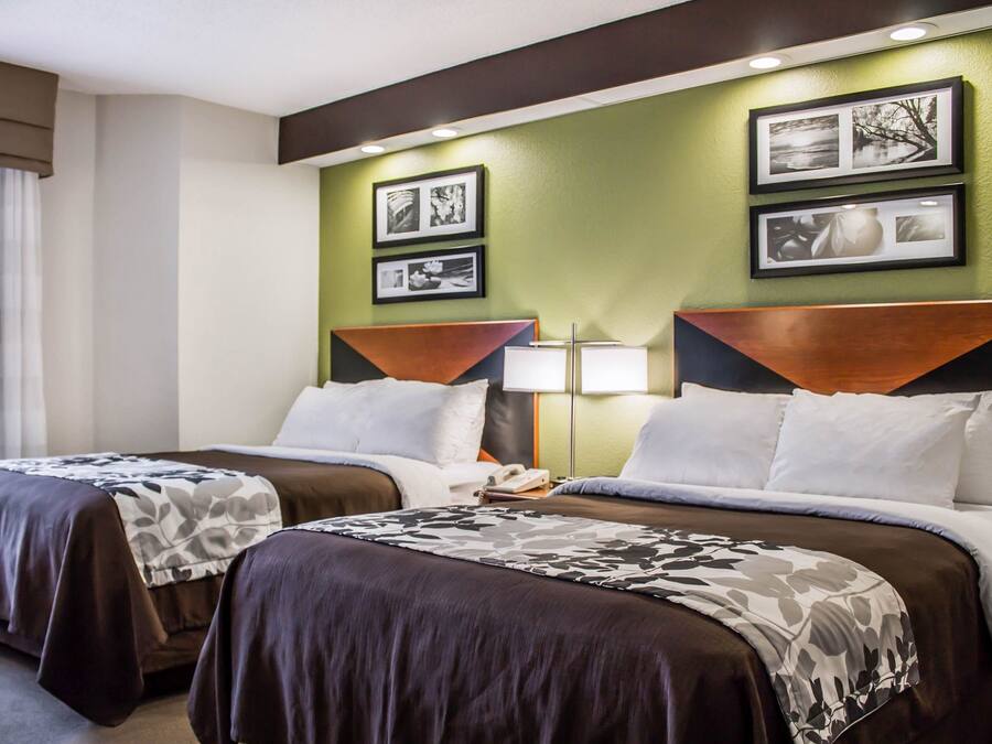 A hotel room with two beds, a nightstand, and a wall-mounted lamp.