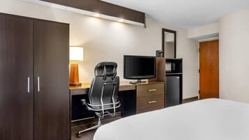 A hotel room with a bed, a desk with a chair, a television, a microwave, and a wardrobe.