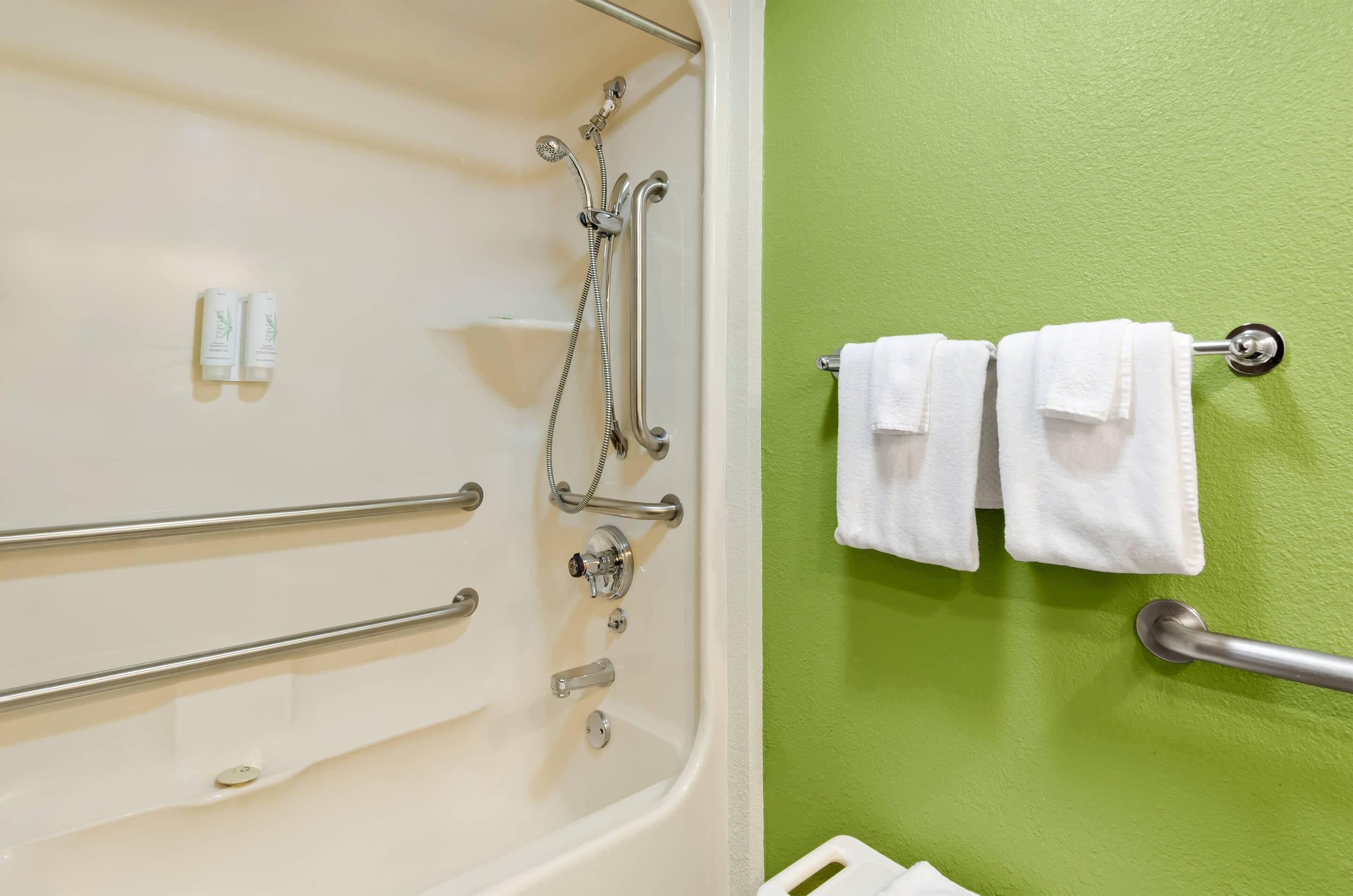 Bagno con vasca, maniglie di sostegno e due asciugamani appesi a un portaservizi.