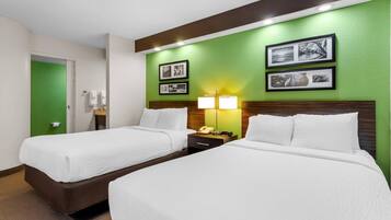 A hotel room with two beds, a green accent wall, framed pictures, a nightstand with a lamp, and a phone.