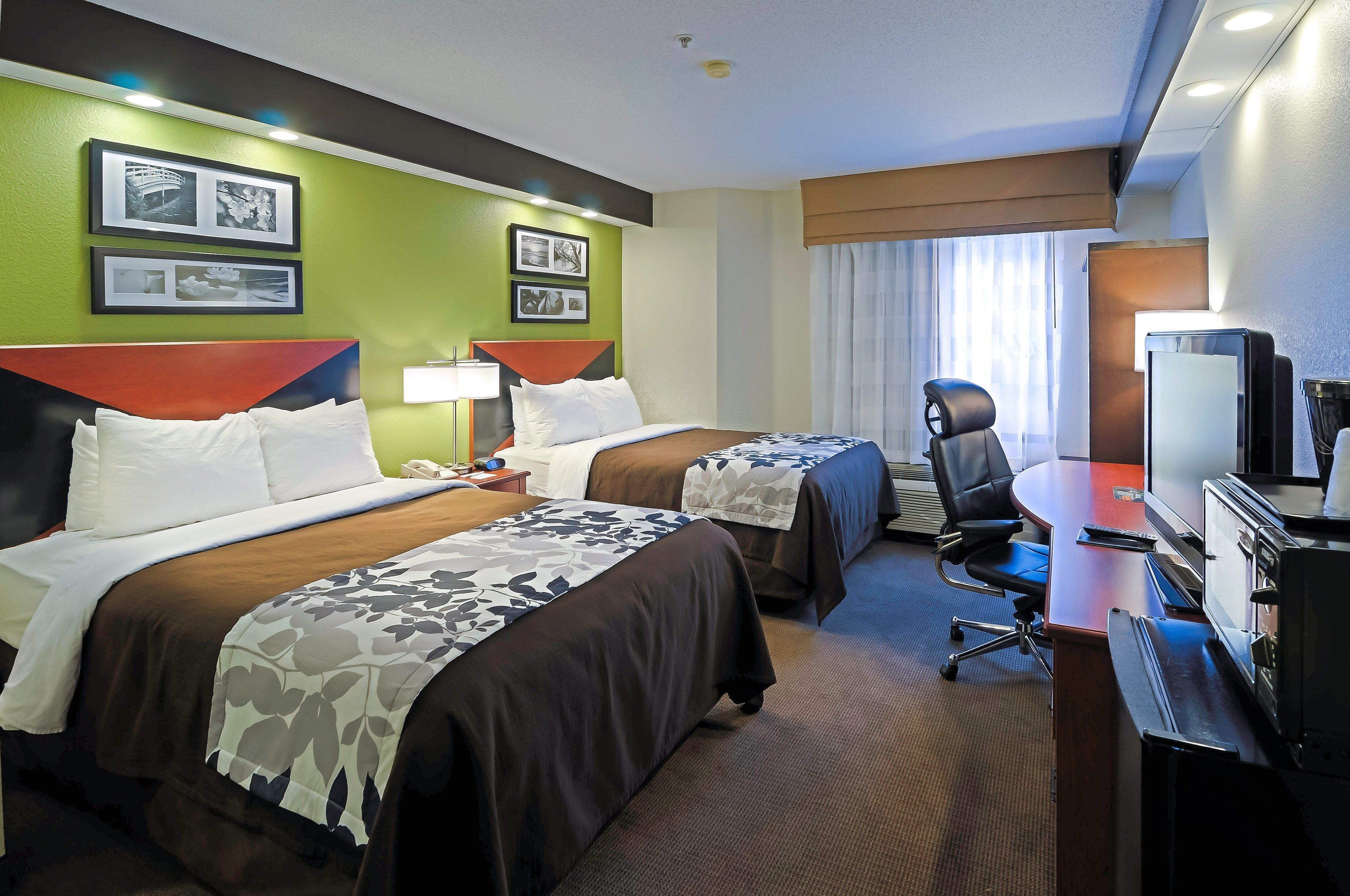 Habitación de hotel con dos camas, un escritorio, una silla, un televisor y cuadros en la pared.