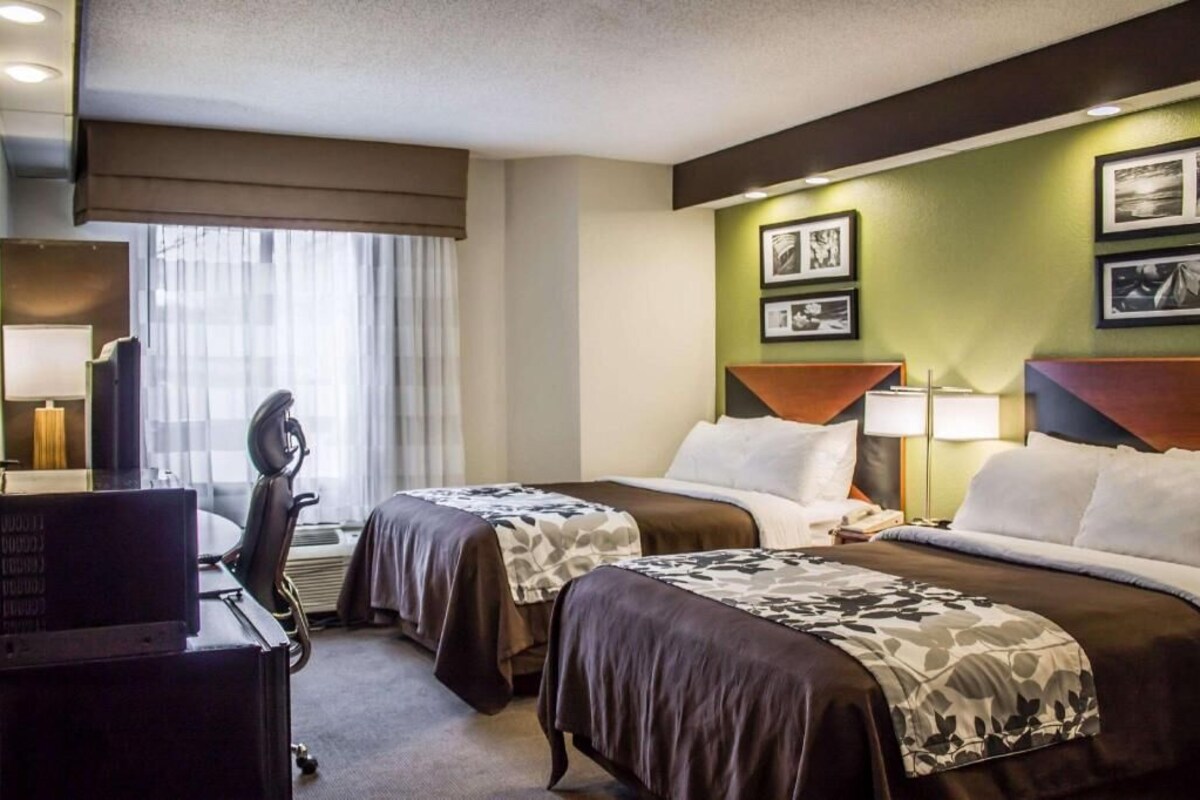A hotel room with two beds, a desk, a chair, a TV, and a window with curtains.