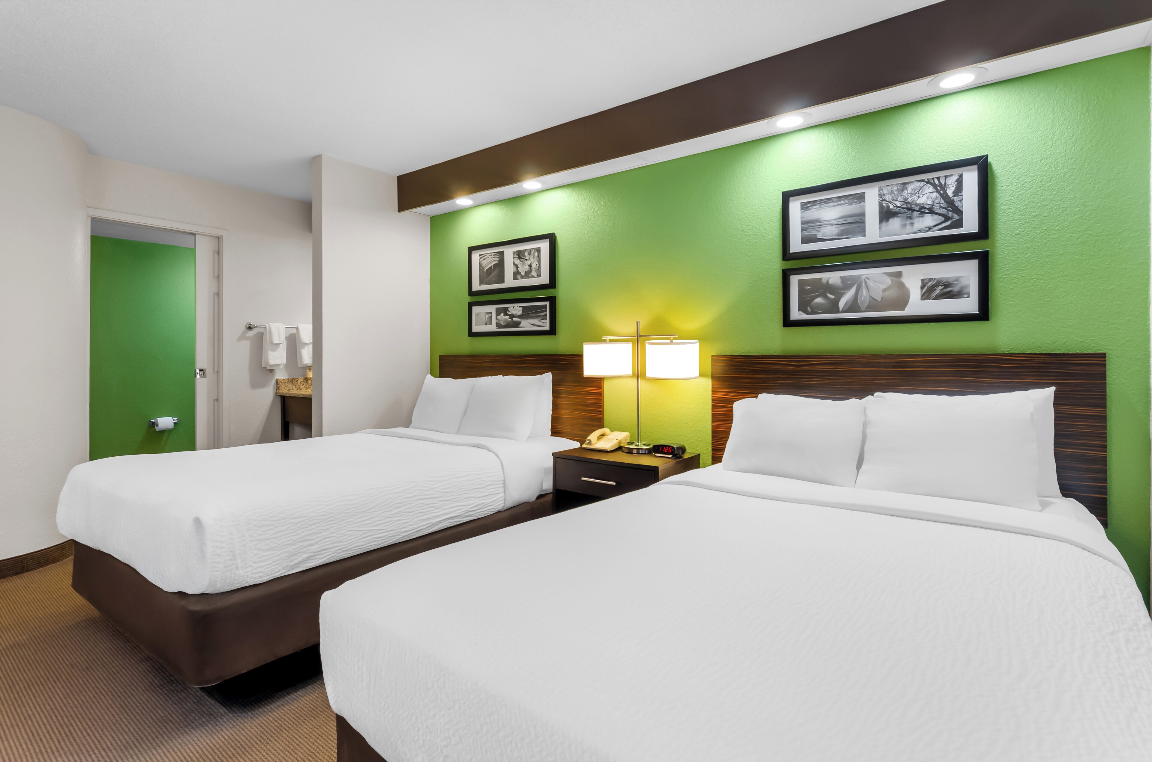 Une chambre d’hôtel avec deux lits, un mur d’accent vert, des tableaux encadrés, une table de chevet avec une lampe et un téléphone.