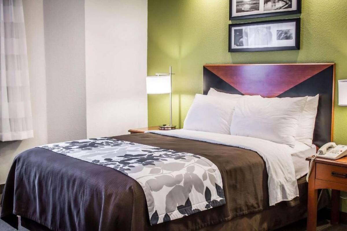 A hotel room with a bed, bedside table, lamp, and a phone.