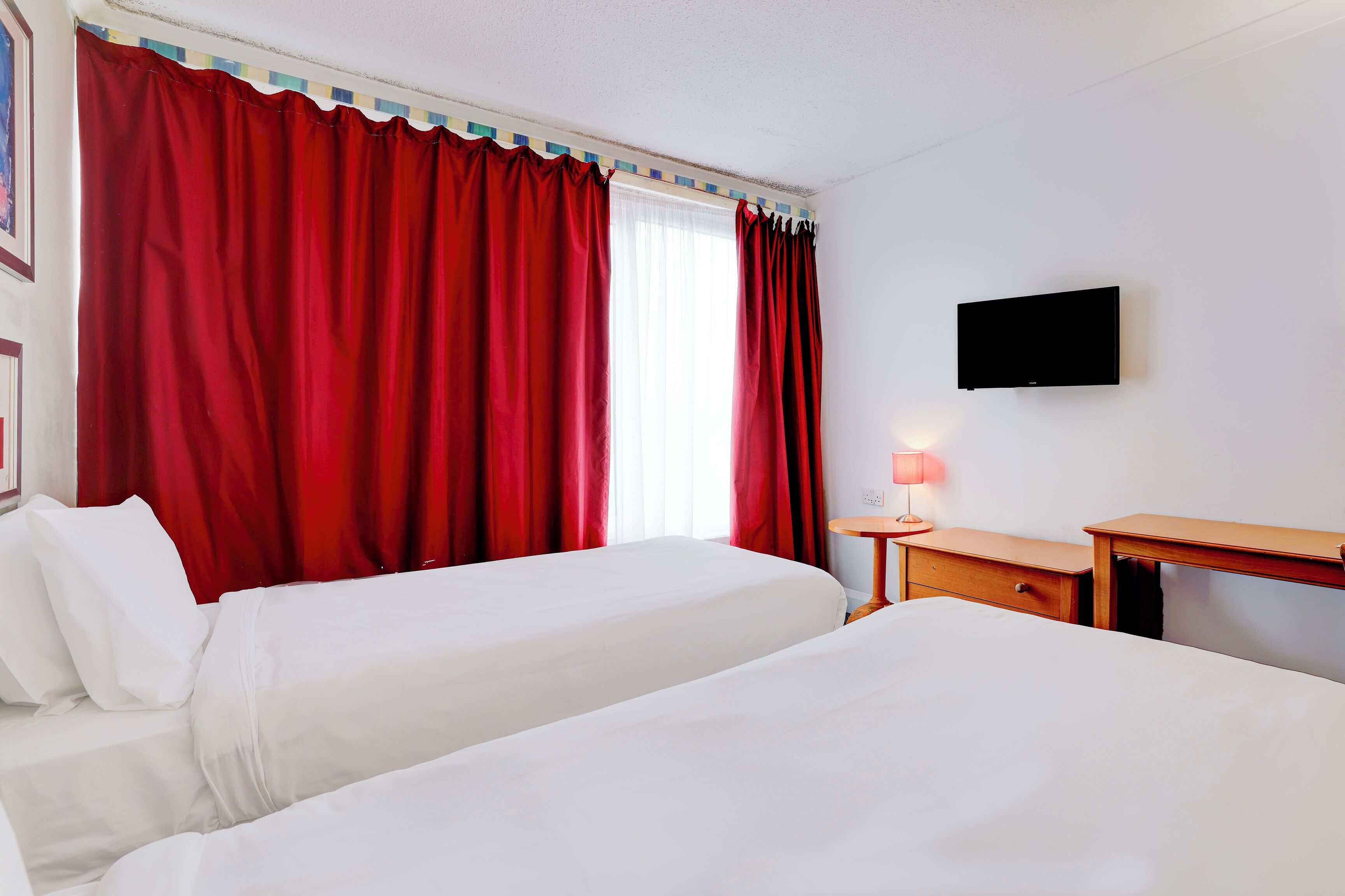 A hotel room with two beds, a TV, a desk, and a lamp.
