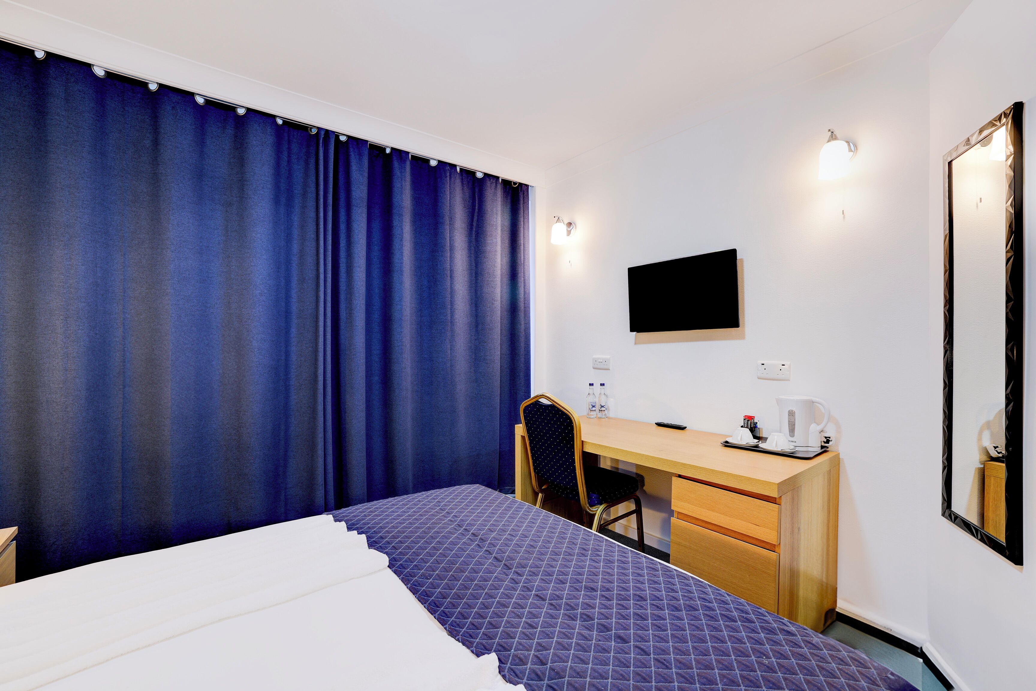 A hotel room with a bed, a desk, a chair, a TV, and a mirror.