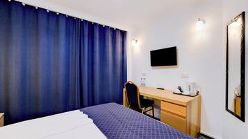 A hotel room with a bed, a desk, a chair, a TV, and a mirror.