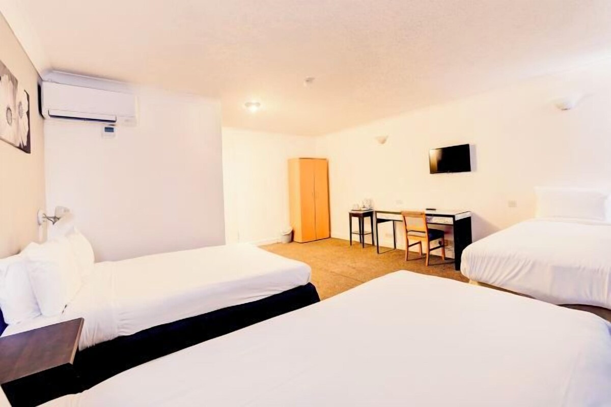 A hotel room with two single beds, a desk with a chair, a television, and an air conditioning unit.