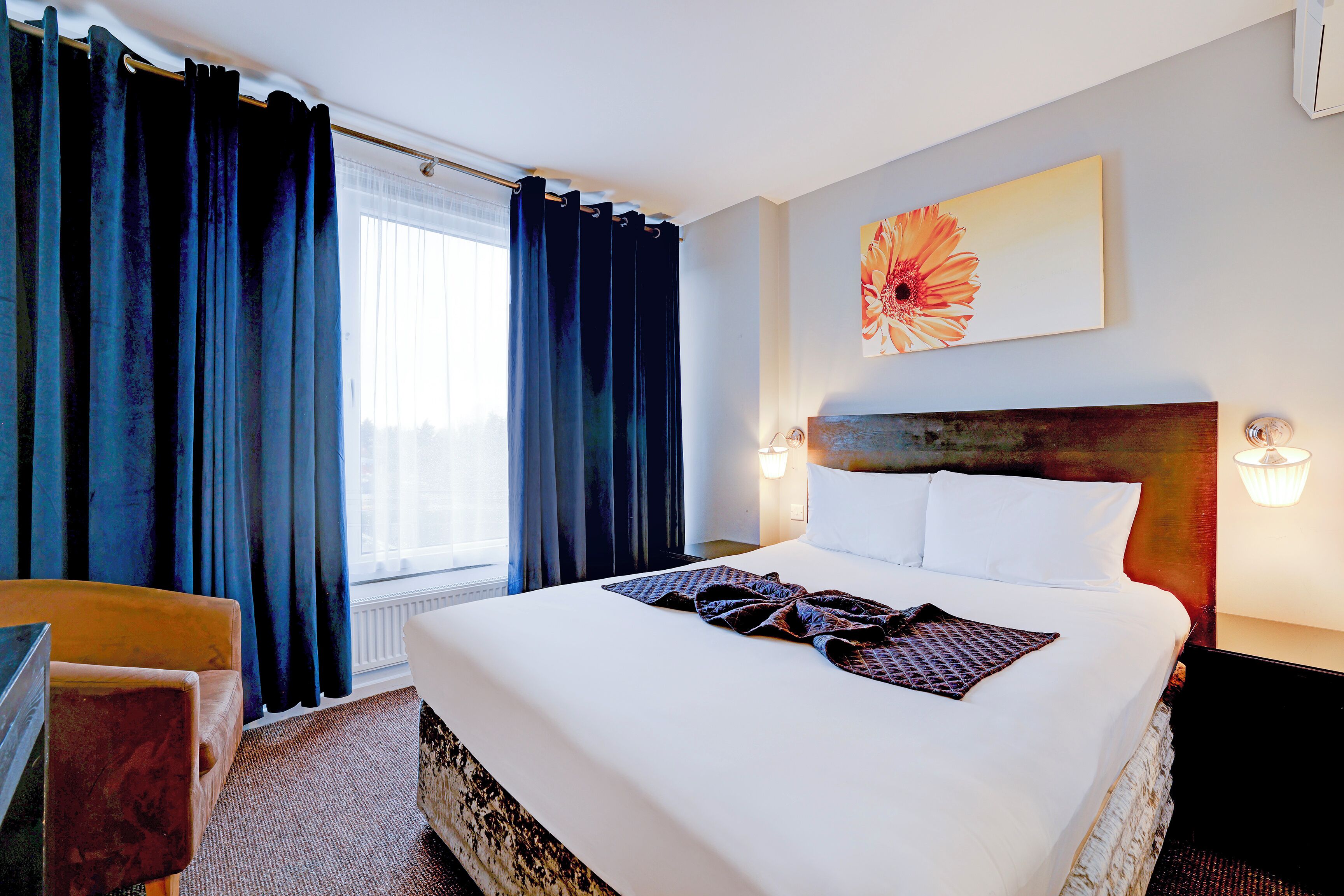 A hotel room with a large bed, a wooden headboard, a painting on the wall, and a window with curtains.