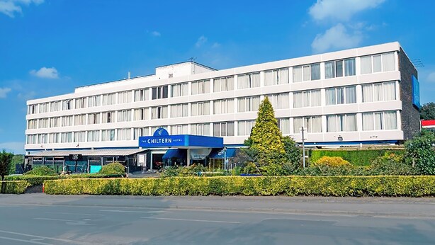 A modern hotel with a flat facade, multiple windows, and a prominent blue sign indicating it is the Chiltern Hotel.