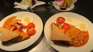 Två tallrikar med frukost bestående av ägg, bönor, tomater och rostat bröd, ställda på ett bord.