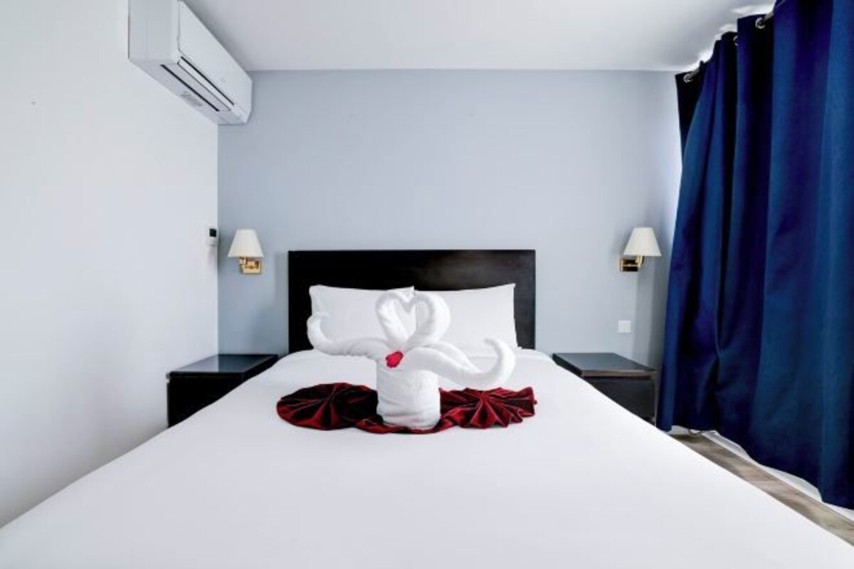 A hotel room with a neatly made bed, a white towel sculpture, and a red pillow.