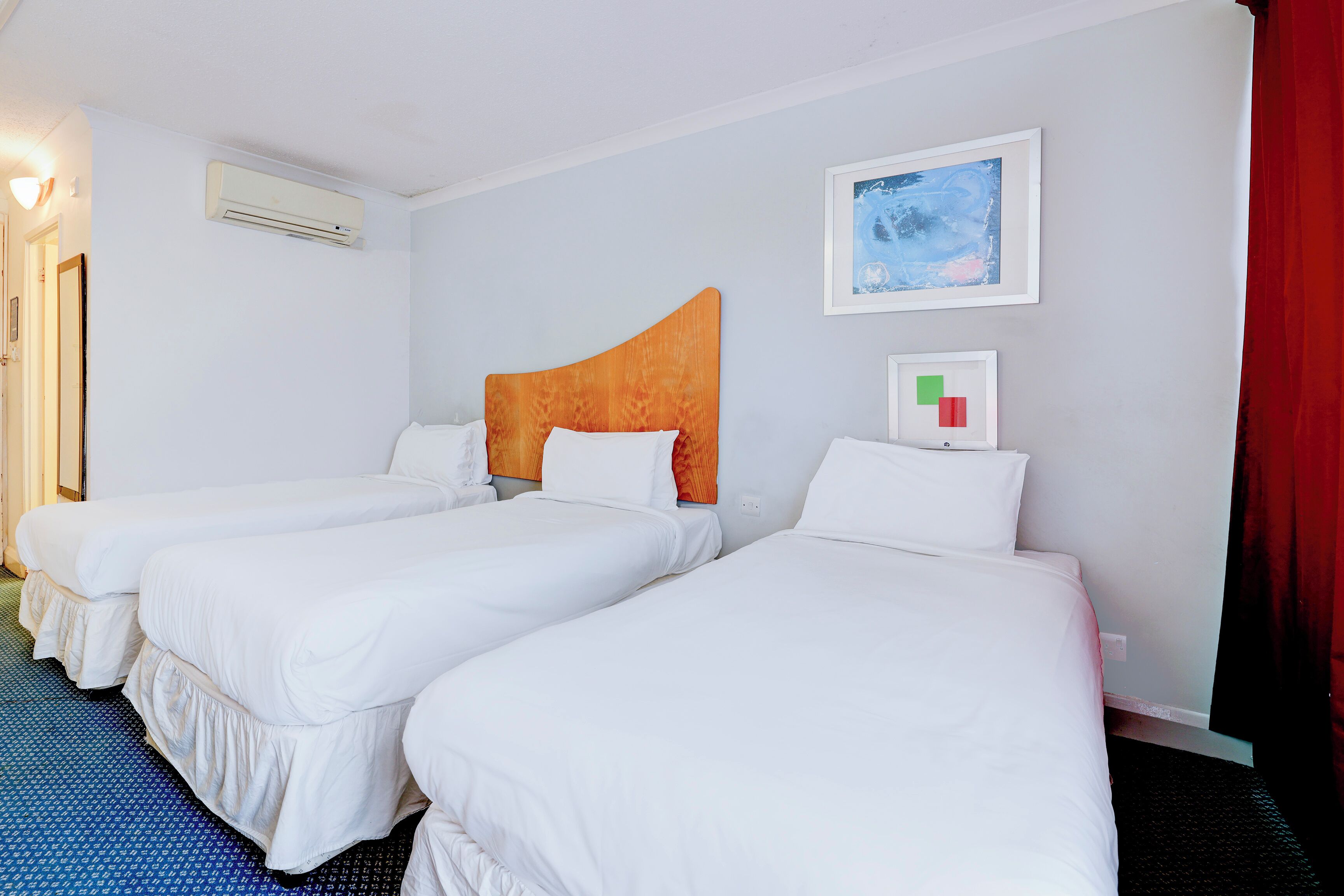 Ein Hotelzimmer mit drei Einzelbetten, einem großen Fenster und einem roten Vorhang.