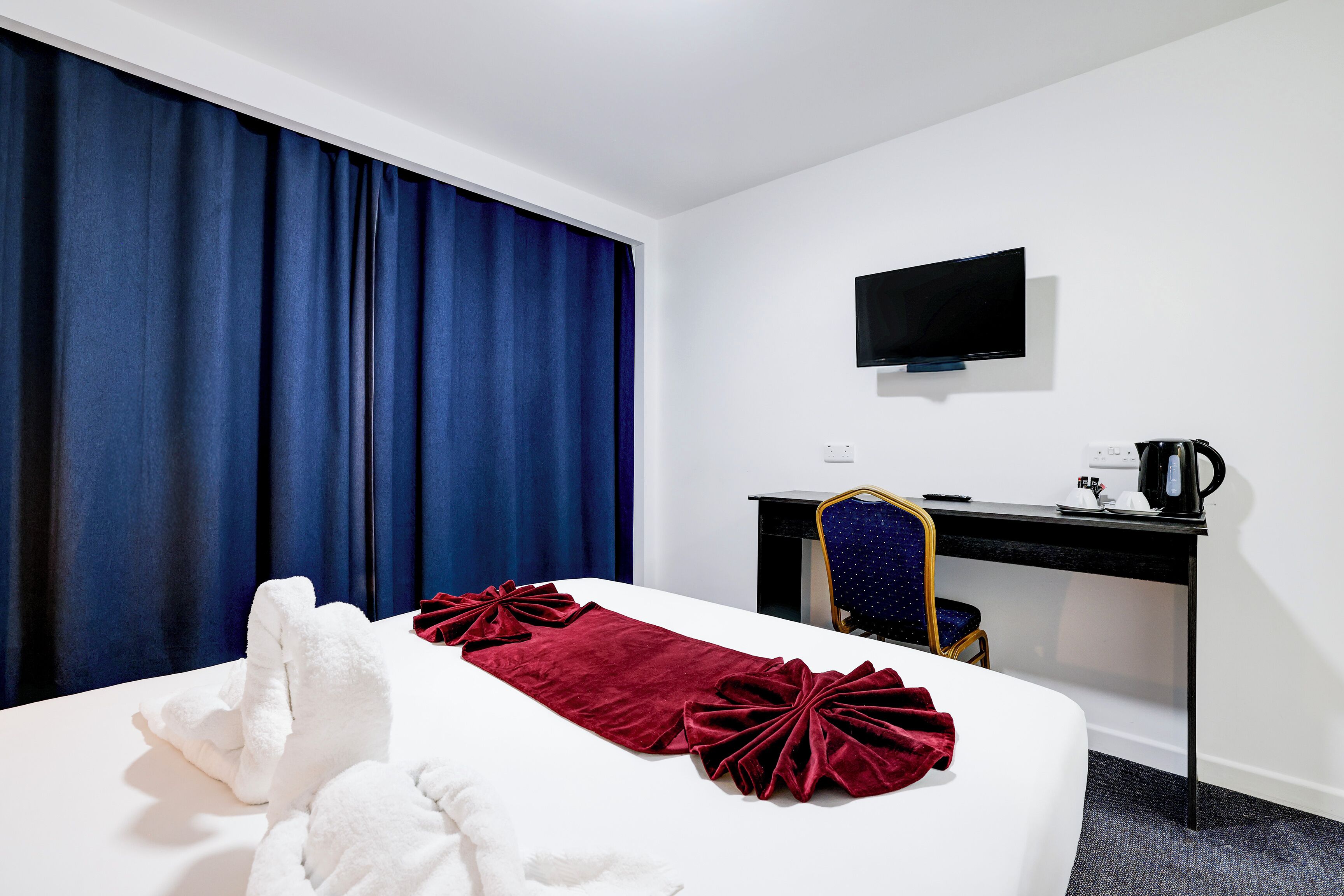 Habitación de hotel con cama, escritorio, silla, televisión y ventana con cortinas.