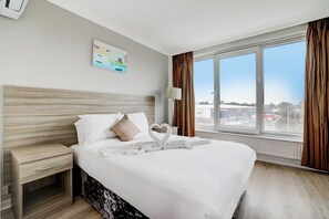 Une chambre d’hôtel avec un grand lit, une table de chevet, une fenêtre avec des rideaux et un tableau au mur.