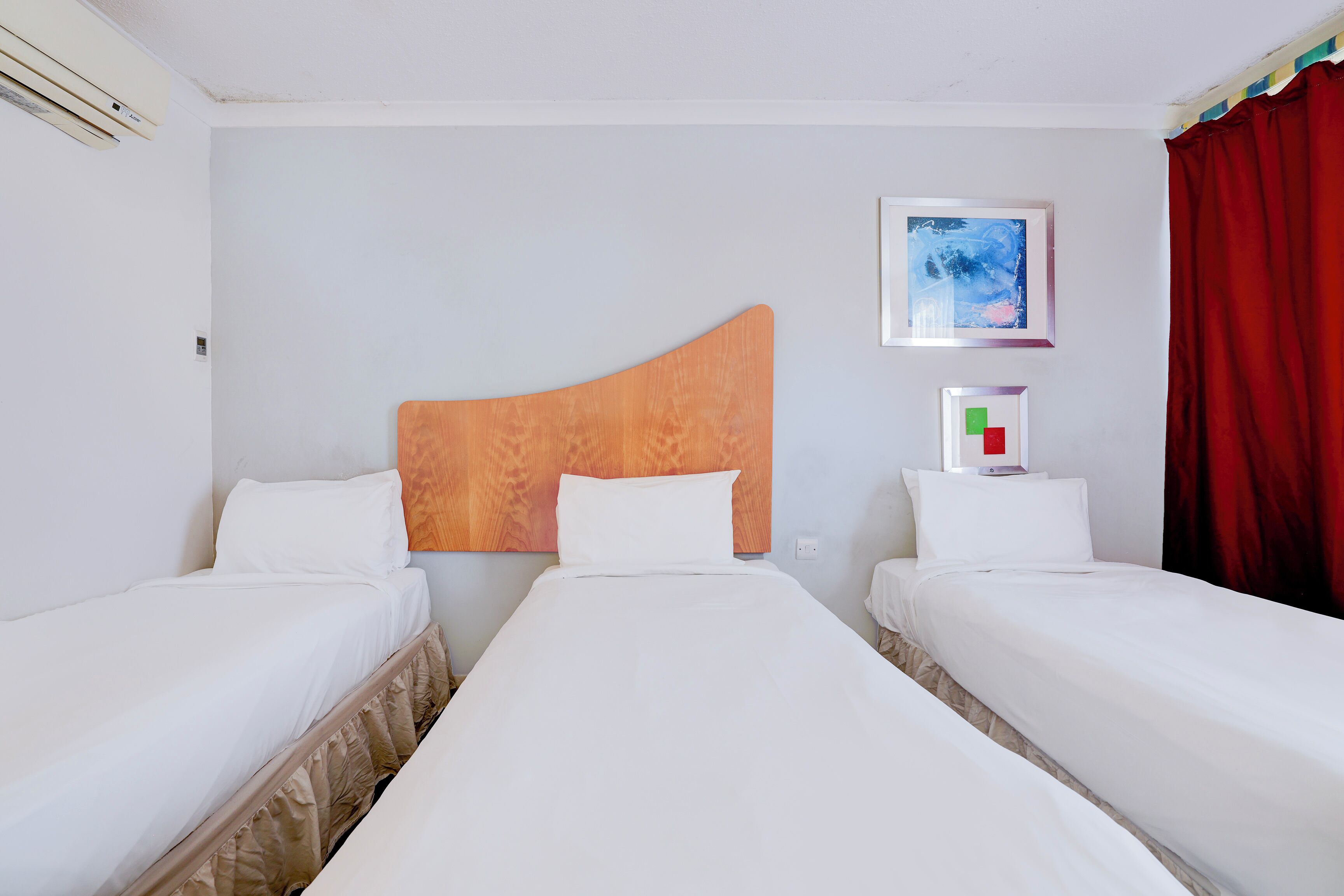 Habitación de hotel con dos camas individuales, cabecera de madera, un cuadro en la pared y una cortina roja.