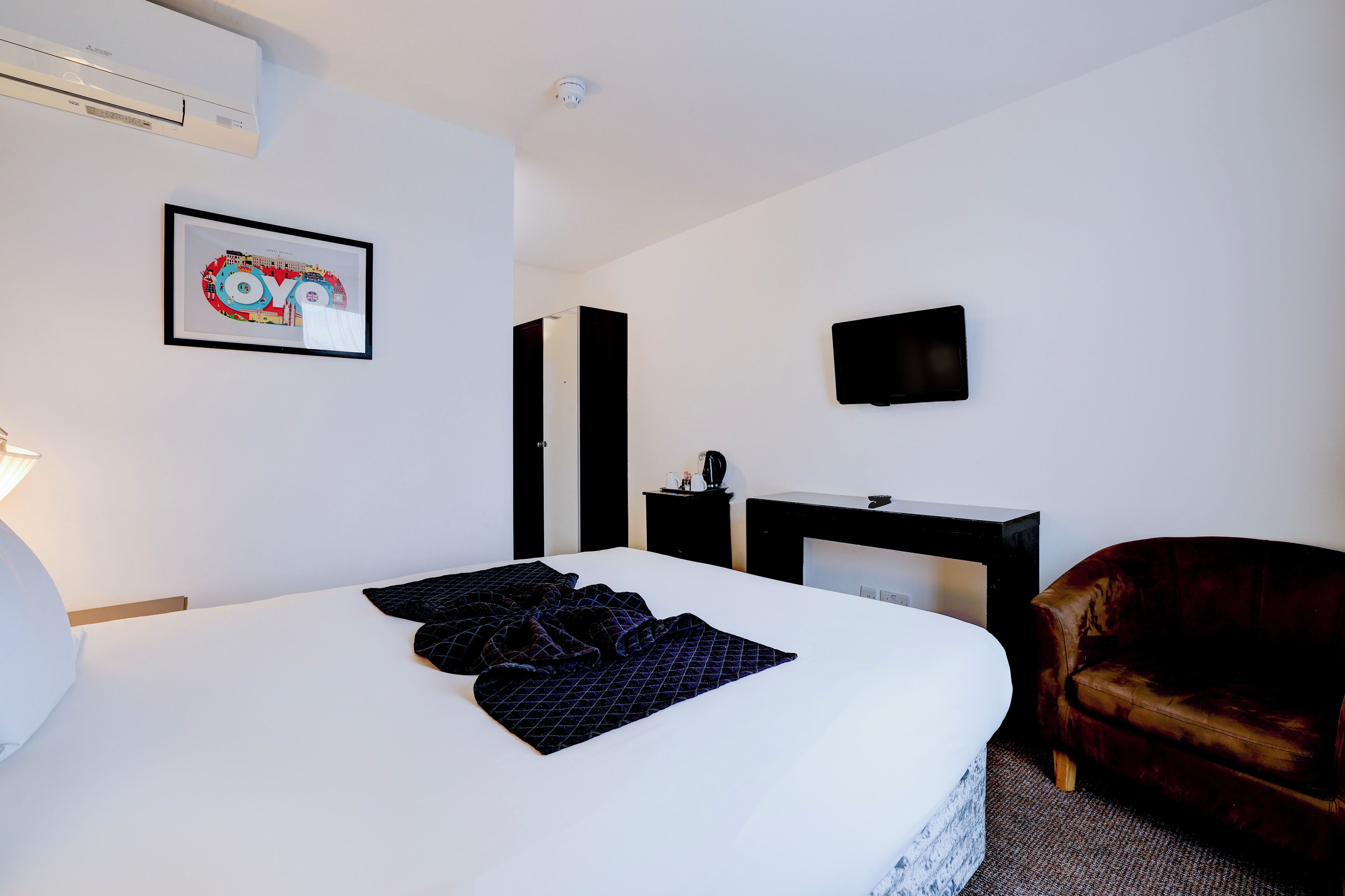 Una habitación de hotel con una cama grande, un escritorio, una silla, un televisor y un cuadro en la pared.