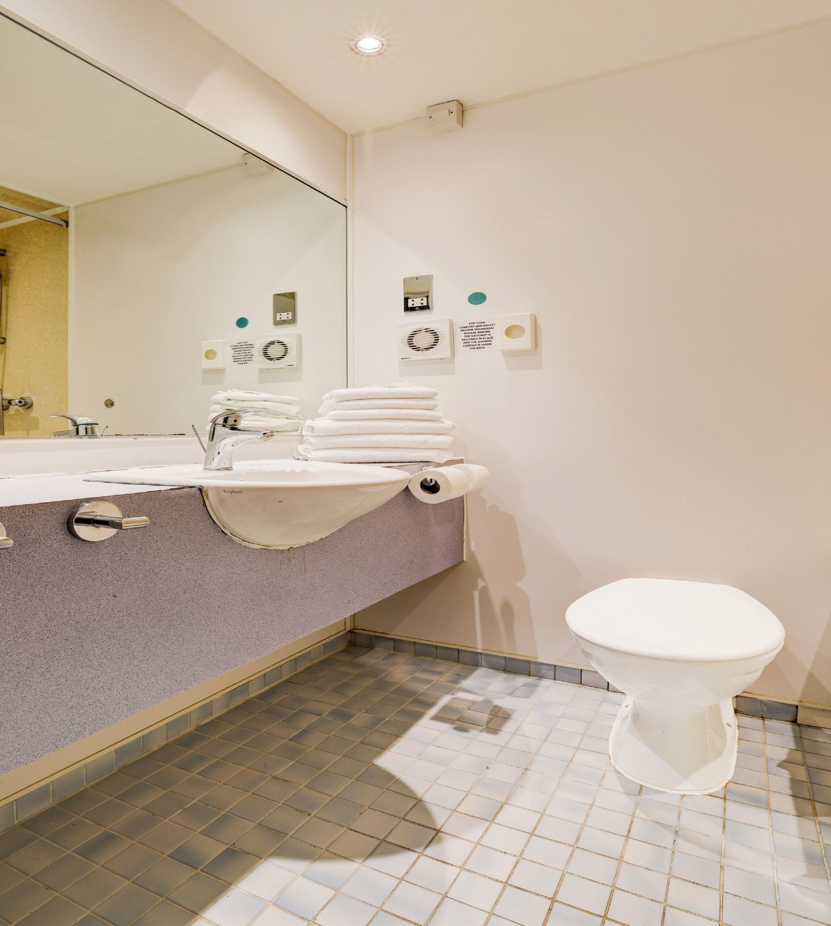 Une salle de bain moderne avec un lavabo, un miroir et des toilettes. Des serviettes sont pliées sur le lavabo et un porte-rouleau de papier toilette est fixé au mur.