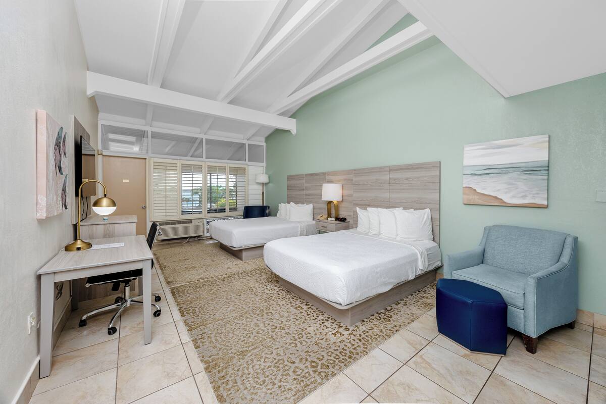 A hotel room with two beds, a desk, a chair, a rug, and artwork on the walls.