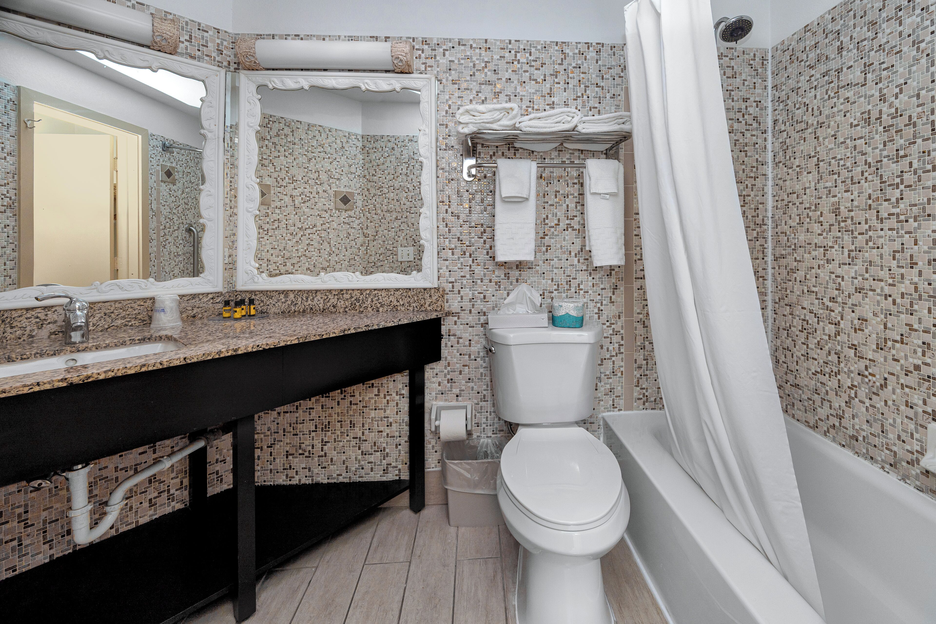 A bathroom with a tiled mosaic wall, a sink with a black countertop, a toilet, and a bathtub with a shower curtain.
