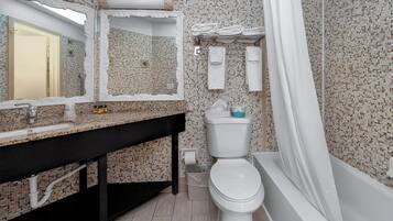 A bathroom with a tiled mosaic wall, a sink with a black countertop, a toilet, and a bathtub with a shower curtain.