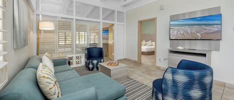 Una sala de estar moderna con un sofá modular, un sillón azul y un televisor de pantalla plana montado en la pared.