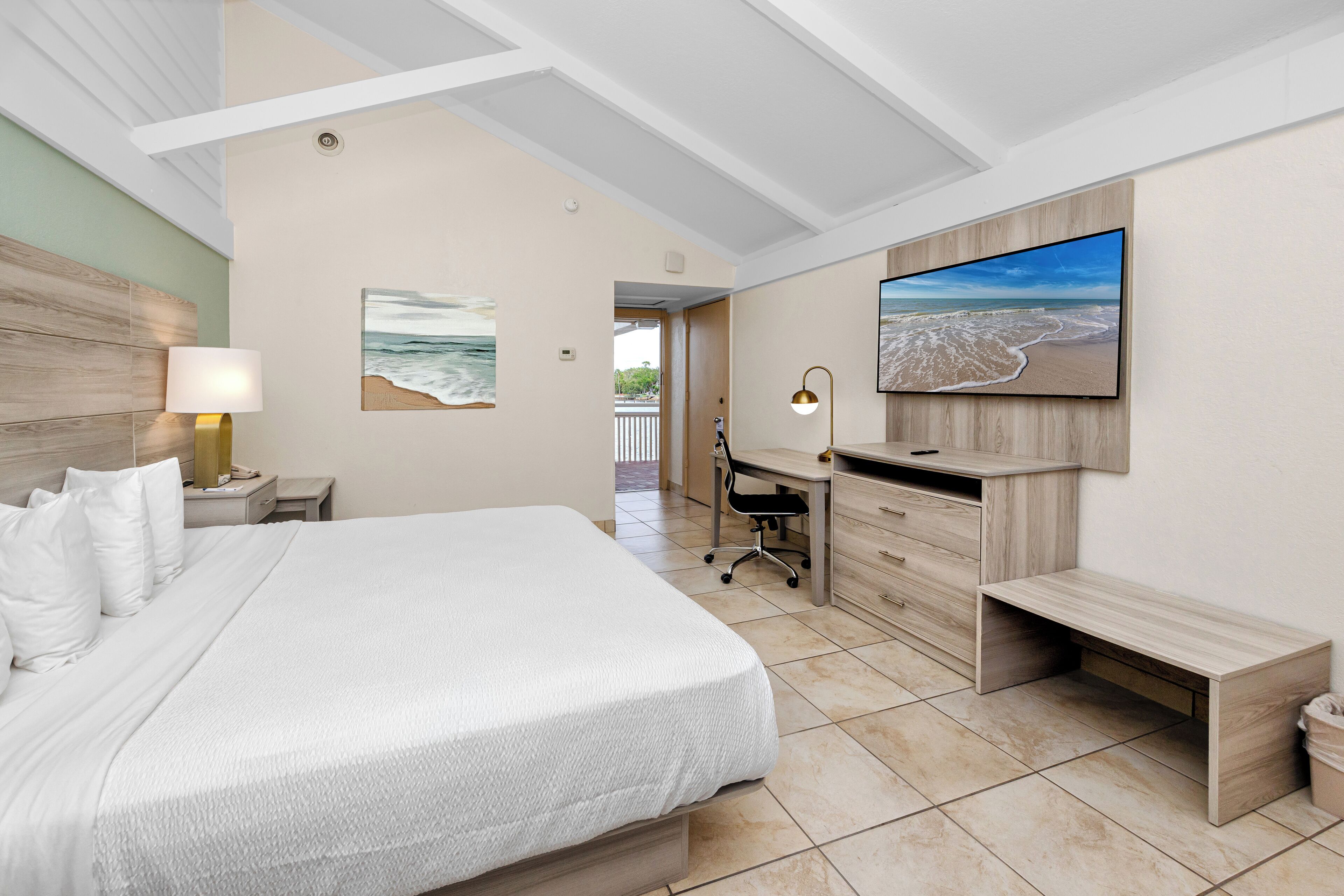 Une chambre d’hôtel avec un lit, un bureau et un grand téléviseur fixé au mur.