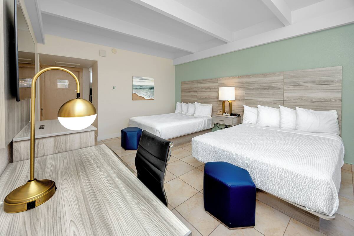 A hotel room with two beds, a desk, a chair, and a TV.