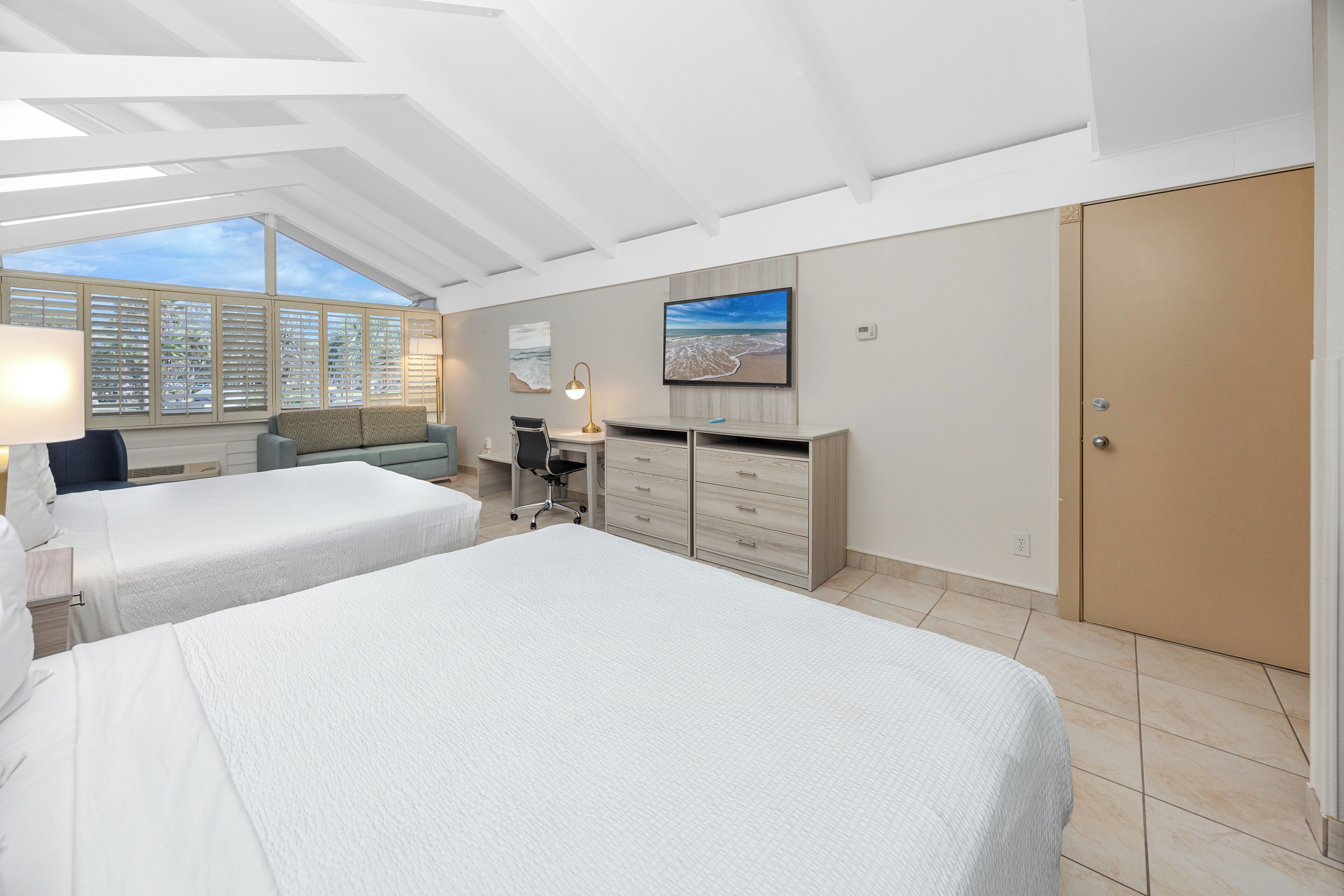 Una habitación de hotel con dos camas, un escritorio, una silla, una lámpara, un televisor y un armario.