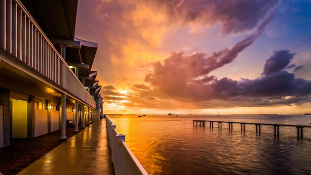 Ein Hotel am Wasser mit einer überdachten Gangway und Blick auf den Sonnenuntergang über dem Wasser.