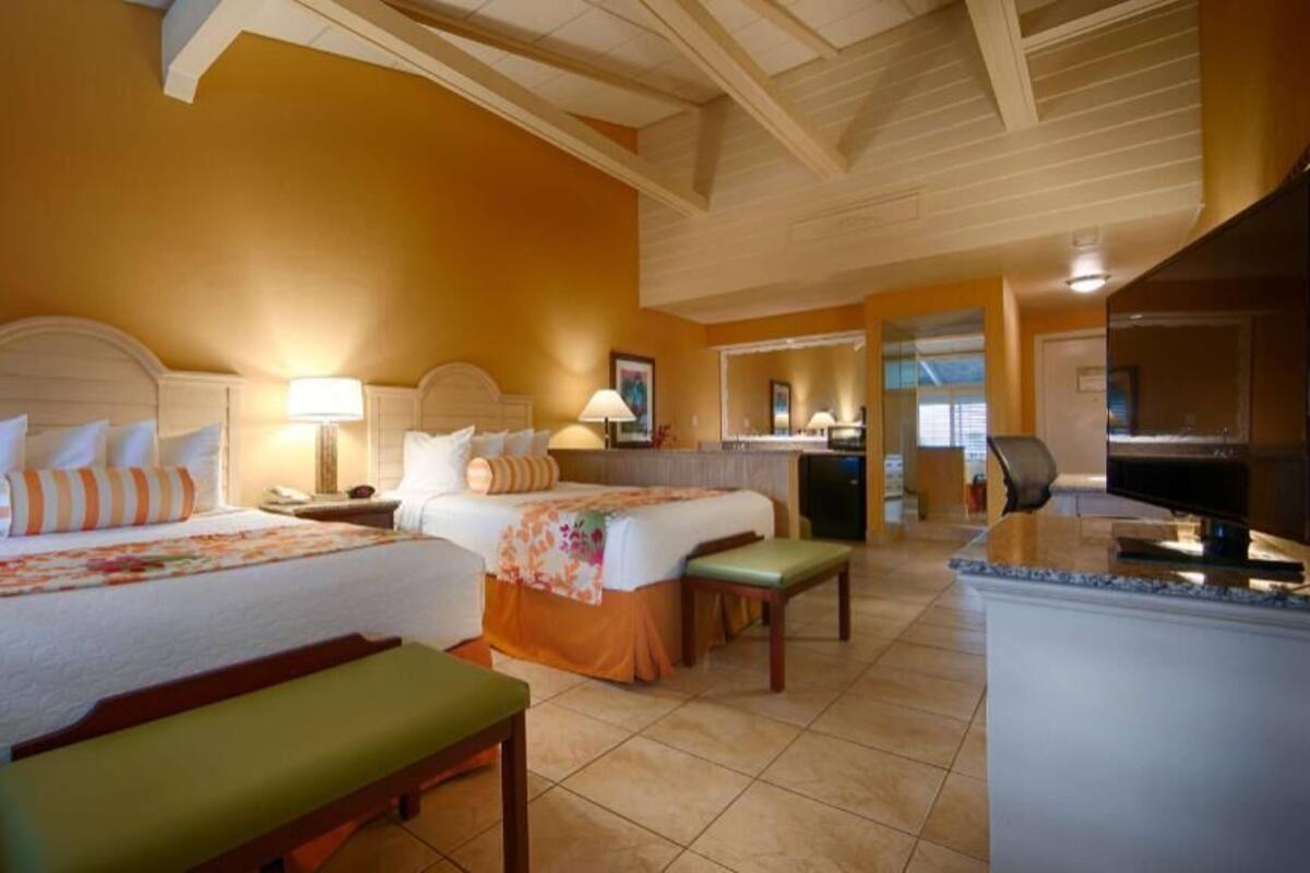 A hotel room with two beds, a kitchenette, a dining area, and a bathroom.