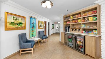 A hallway with seating, artwork, and a snack bar with various food items.
