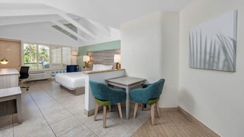 A modern hotel room with a bed, desk, and chairs, a small table, and a painting on the wall.