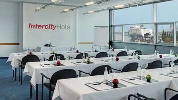 Una sala de conferencias en el Intercity Hotel con mesas dispuestas para reuniones, una pizarra blanca y vistas a la ciudad.