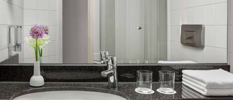 A modern bathroom with a large mirror, a sink, a glass shower enclosure, and a towel rack.