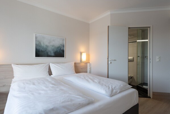 A hotel room with a large bed, a painting on the wall, and a bathroom visible through an open door. - IntercityHotel Kiel (Kiel)