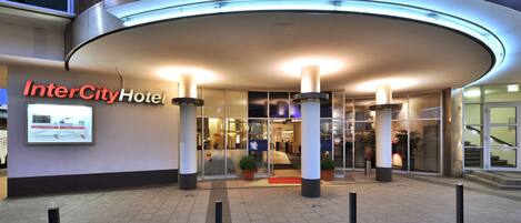 Der Eingang des InterCity Hotels mit modernem Design, der eine geschwungene Fassade, Glastüren und ein Schild zeigt.