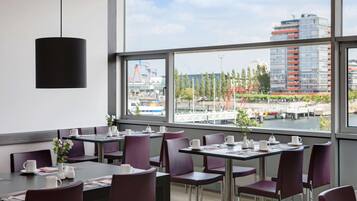 A modern dining area with tables and chairs, large windows offering a view of a cityscape.