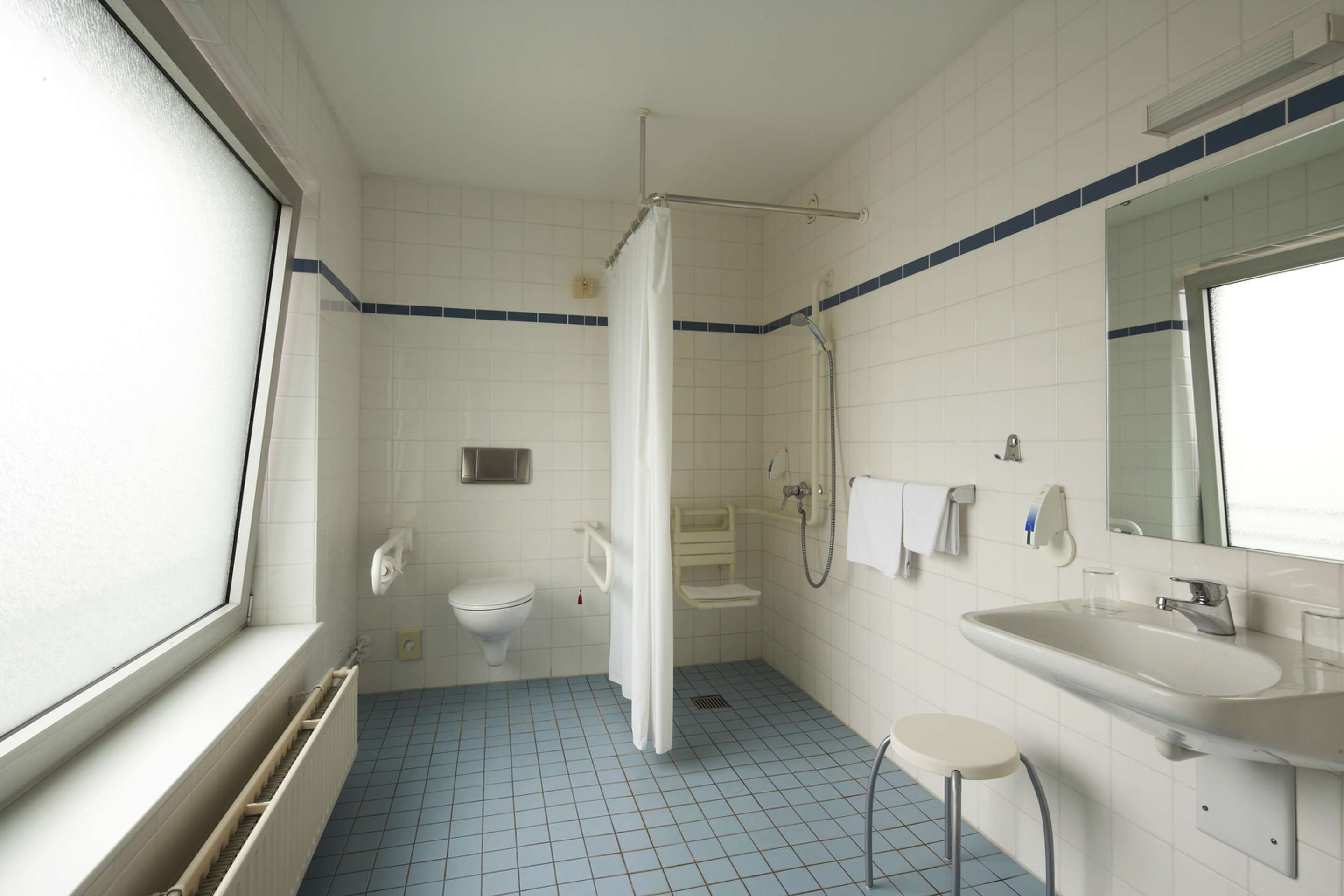 A bathroom with a toilet, sink, shower, and a window.