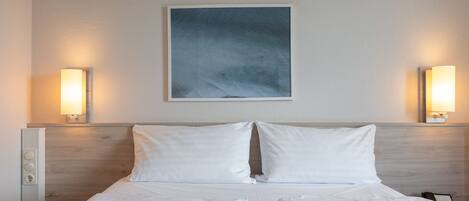 Habitación de hotel con una cama, dos lámparas de noche, una obra de arte en la pared y una mesita de noche con lámpara.