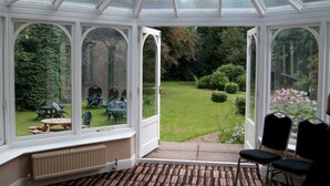 A conservatory with a glass roof, a garden view, and a seating area with chairs and a table. - Cobden Hotel Birmingham (Birmingham)